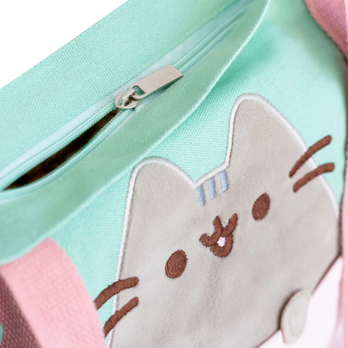 Una borsa tote verde menta con cerniera. Presenta un design a forma di gatto. Sono visibili delle cinghie rosa.