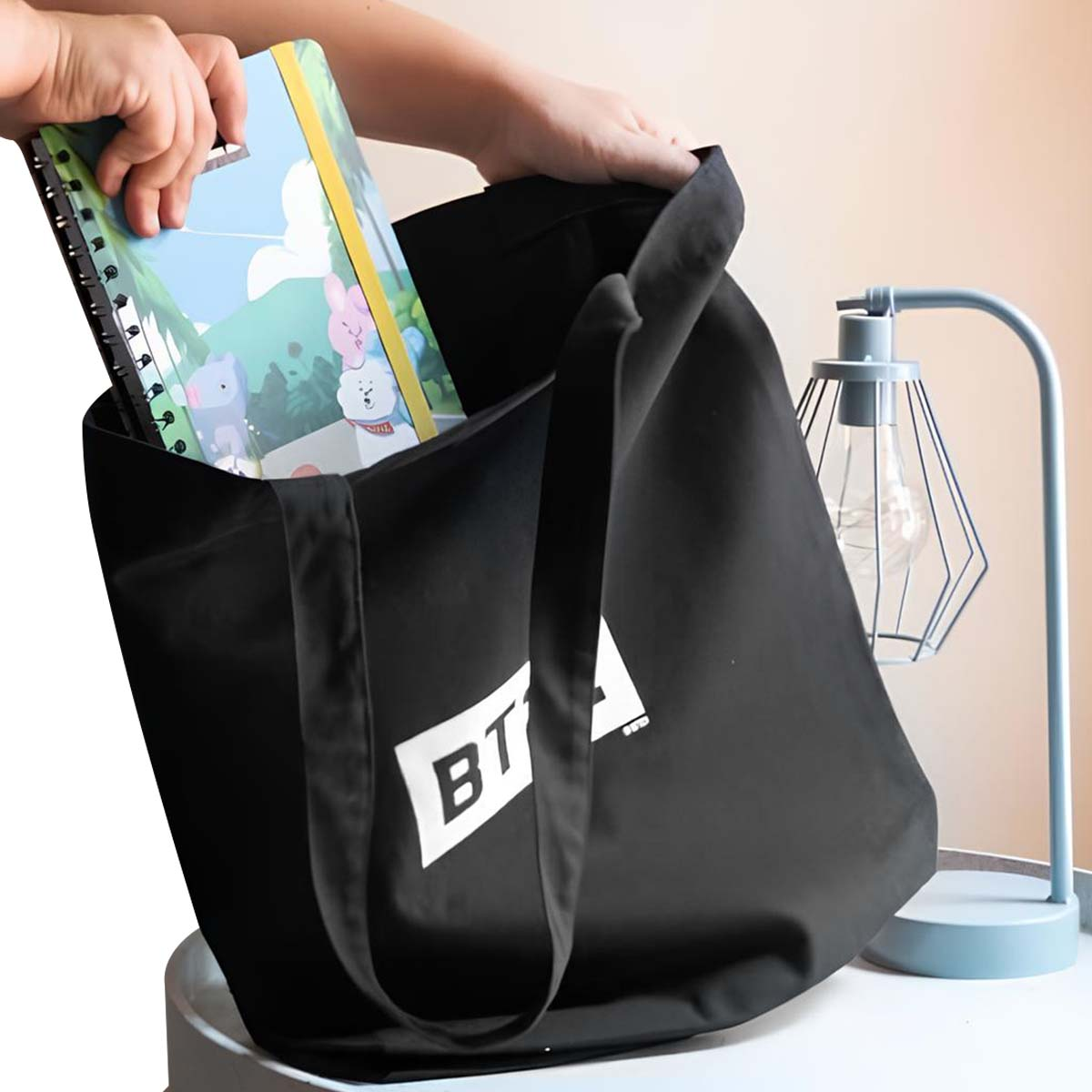 Mani che mettono un taccuino in una borsa nera con le lettere 'BT'. A destra c'è una lampada blu.