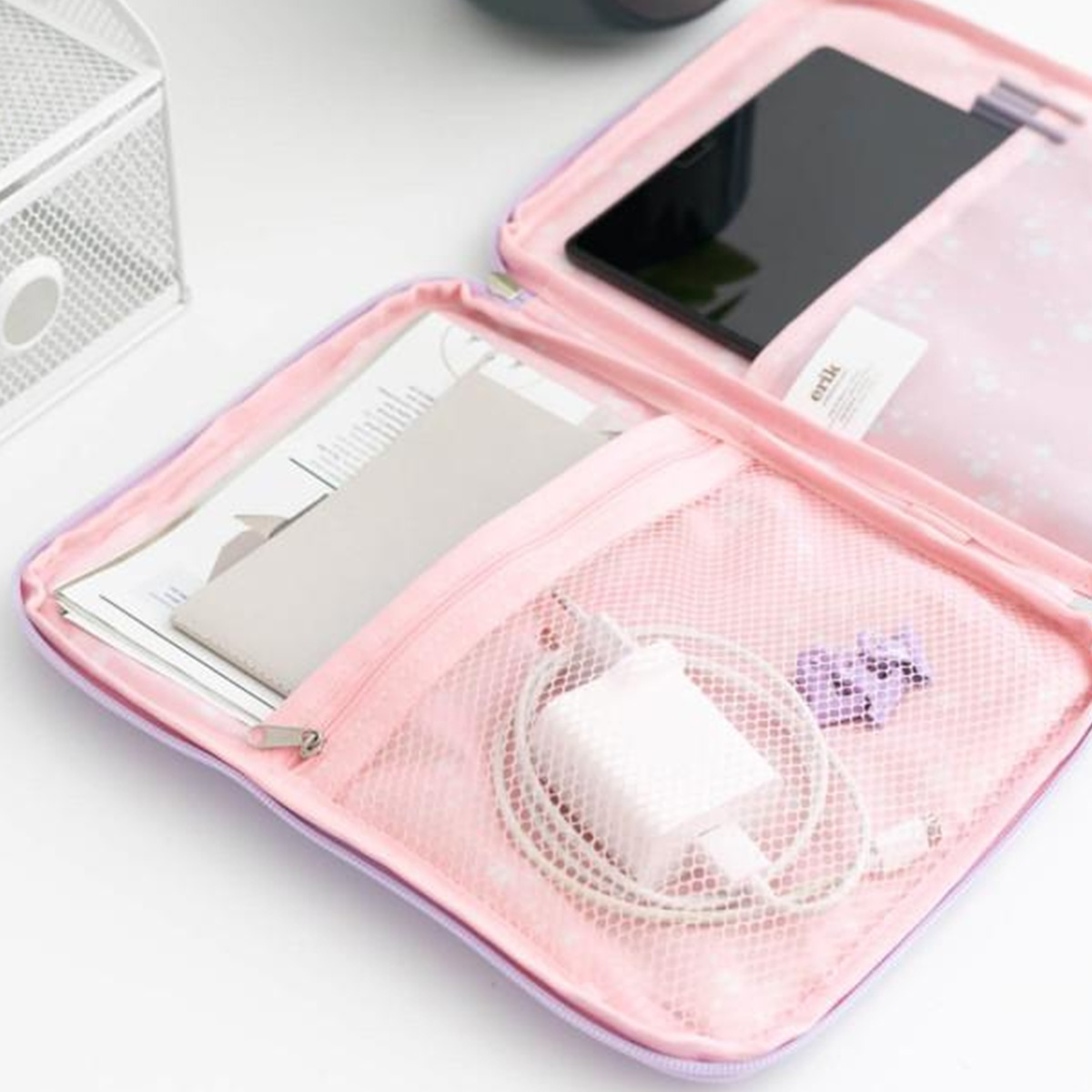 Custodia rosa aperta con tablet, documenti, caricabatterie e piccole decorazioni viola. Tasca a rete metallica bianca.
