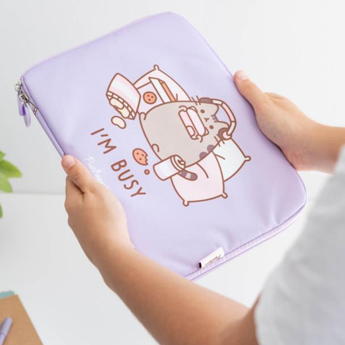 Una persona tiene in mano una custodia viola per laptop con un disegno di un gatto dei cartoni animati. Il gatto è circondato da cuscini e biscotti.