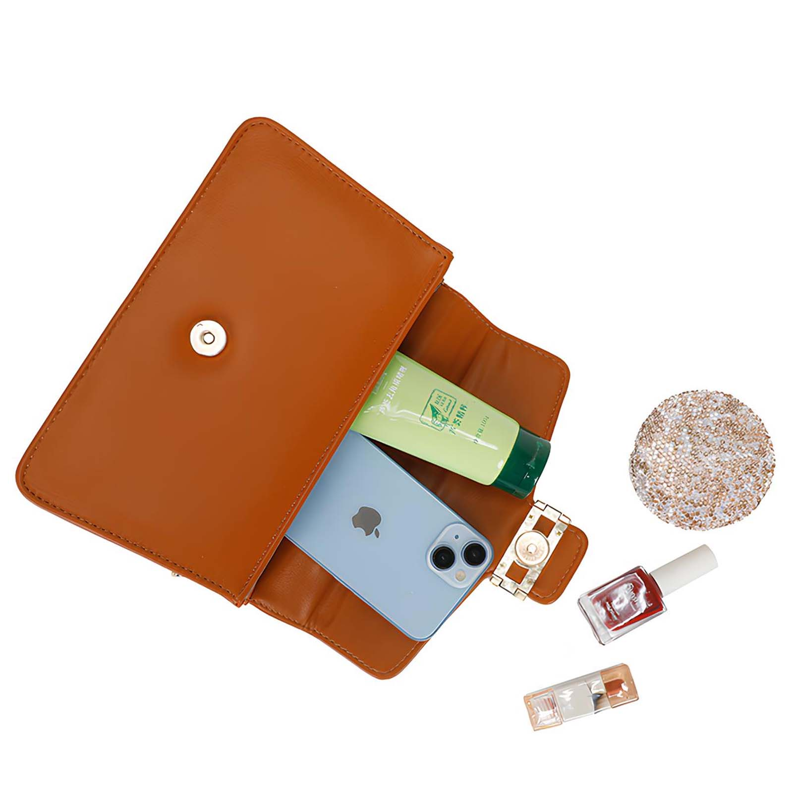 Bolso marrón abierto con teléfono, tubo de crema, reloj, esmalte de uñas y purpurina. Fondo blanco.