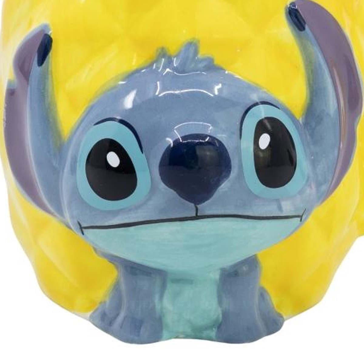 Eine Stitch-förmige Tasse. Die Tasse ist blau mit großen Augen und Ohren, vor einem gelben Hintergrund, der einer Ananas ähnelt.