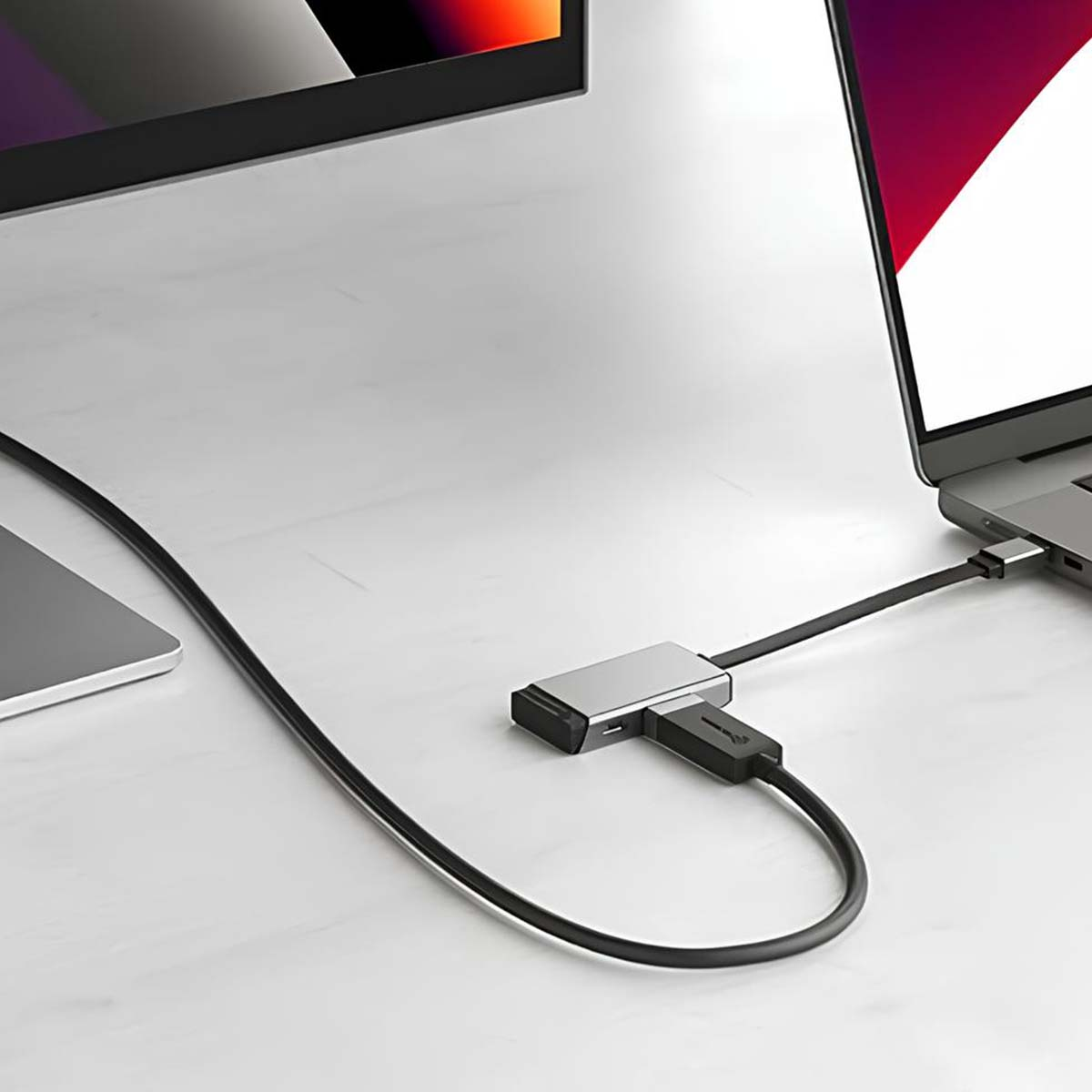 Ein Laptop, der über Kabel mit einem Monitor und einem Hub auf einer weißen Oberfläche verbunden ist. Der Laptop-Bildschirm zeigt einen bunten Farbverlauf.