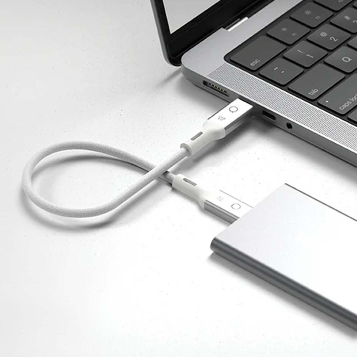 Laptop collegato a un disco rigido esterno argento tramite cavo USB-C bianco. La tastiera del laptop è visibile.
