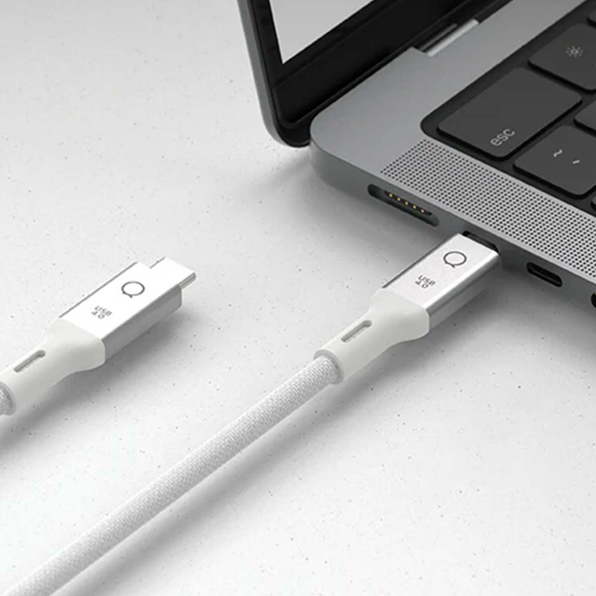 Un cavo USB-C bianco è collegato a un laptop. Il cavo ha una trama in tessuto. Un'altra estremità del cavo è scollegata.