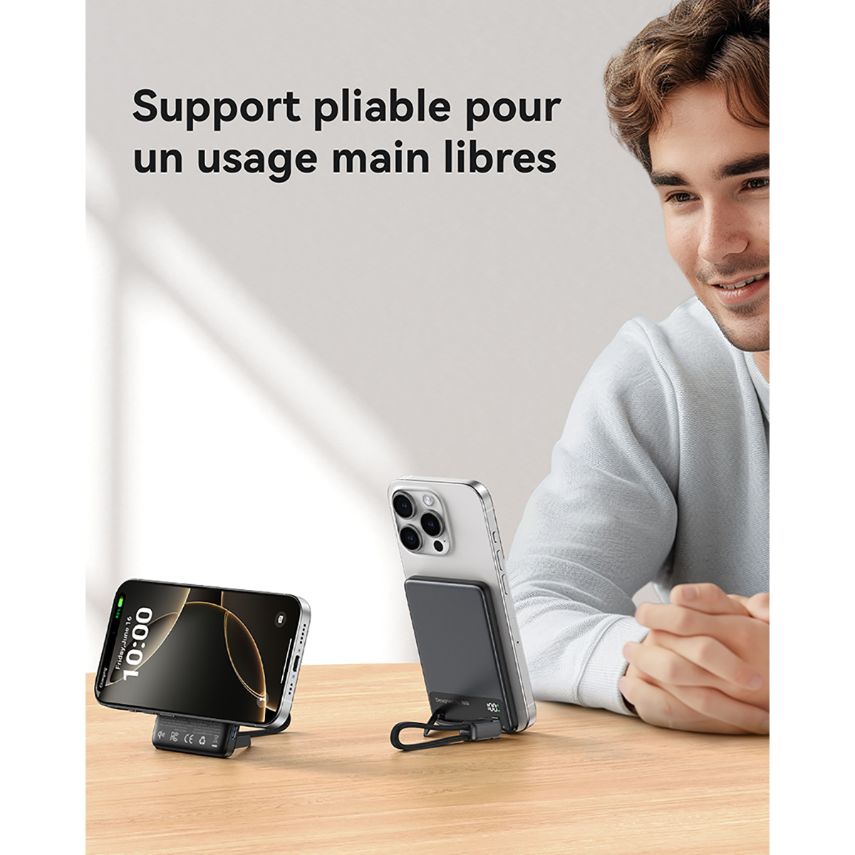 Ein Mann lächelt neben zwei Handys auf einem Holztisch. Ein Telefon steht, das andere hat eine Powerbank.