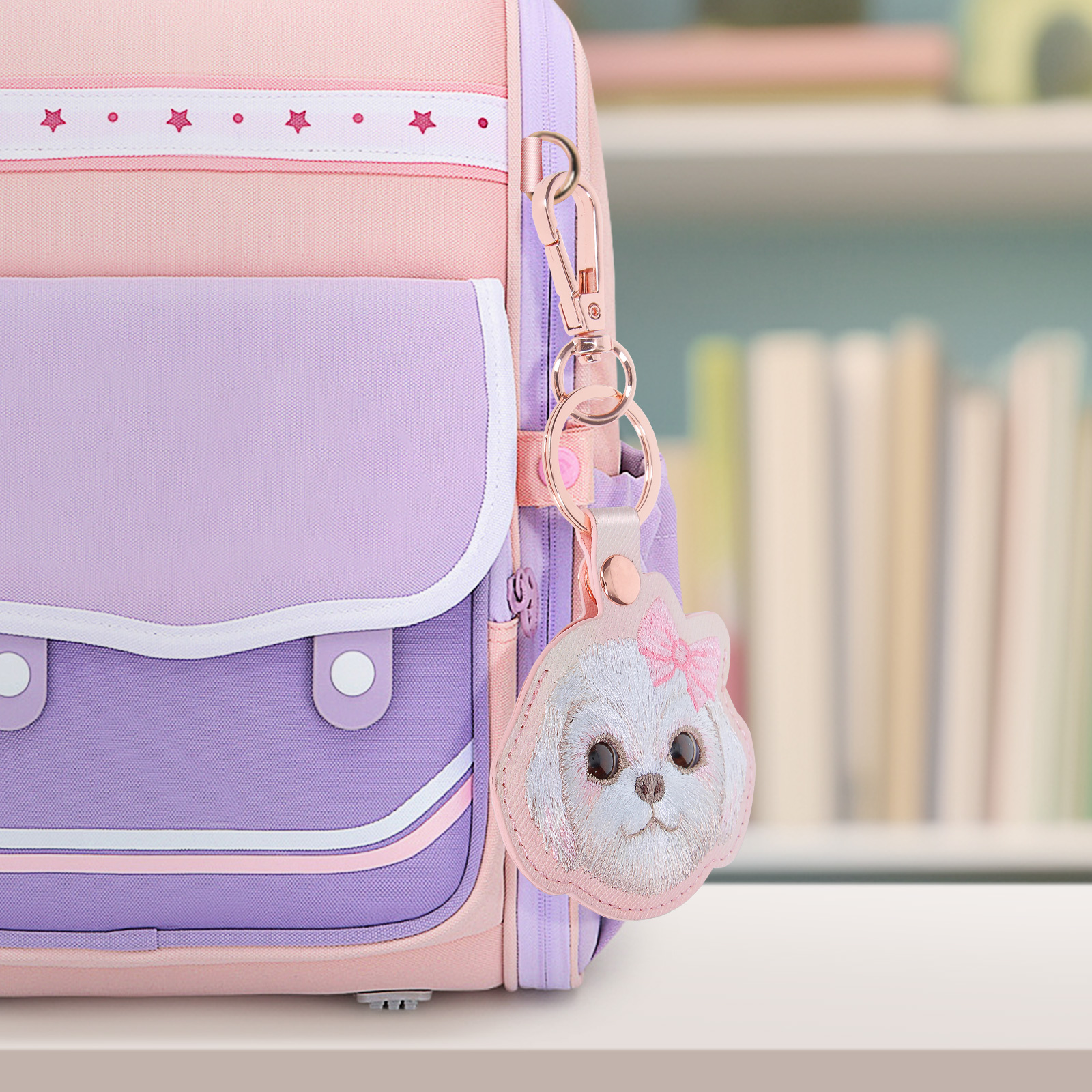 Uno zaino rosa e viola con un portachiavi a forma di cane. Libri sullo sfondo sfocato. Il portachiavi ha un fiocco rosa.