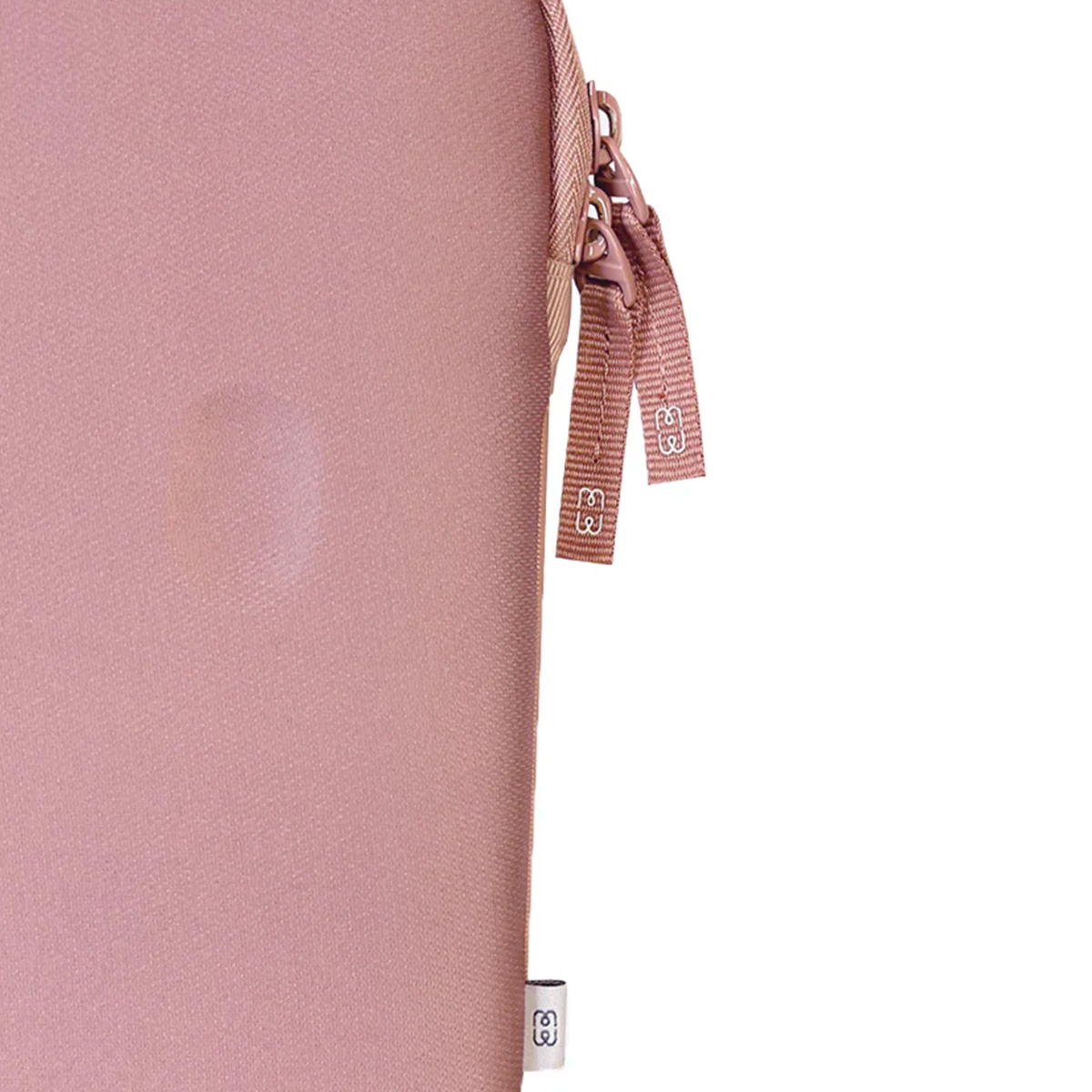 Primo piano di una custodia rosa con cerniera e piccole etichette. Lo sfondo è bianco.