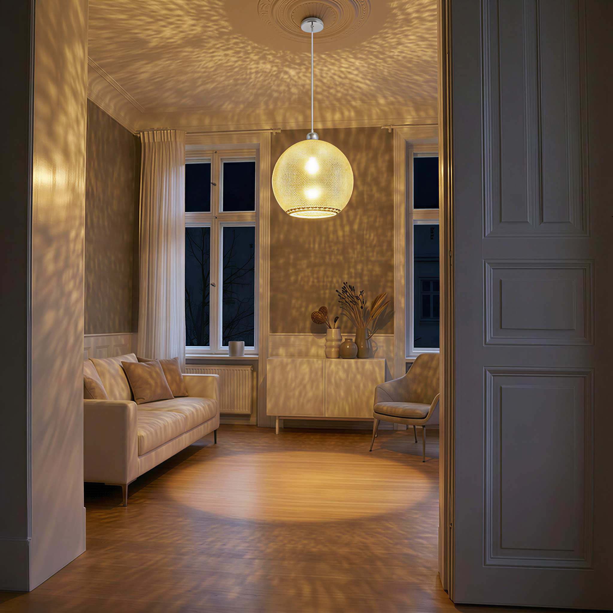 Ein Raum mit einer Hängelampe, die Lichtmuster wirft. Sofa, Schrank und Sessel sind sichtbar. Fenster zeigen eine dunkle Nacht.