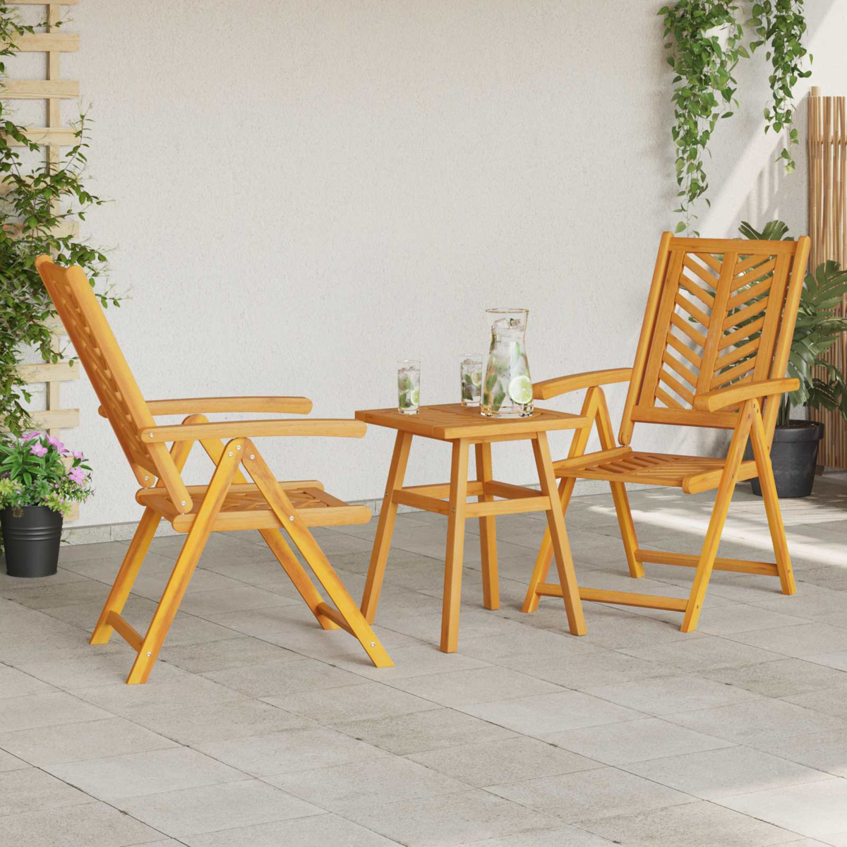 Set da patio in legno con due sedie e un tavolino. Ci sono bevande con lime sul tavolo. Piante e un muro bianco sullo sfondo.