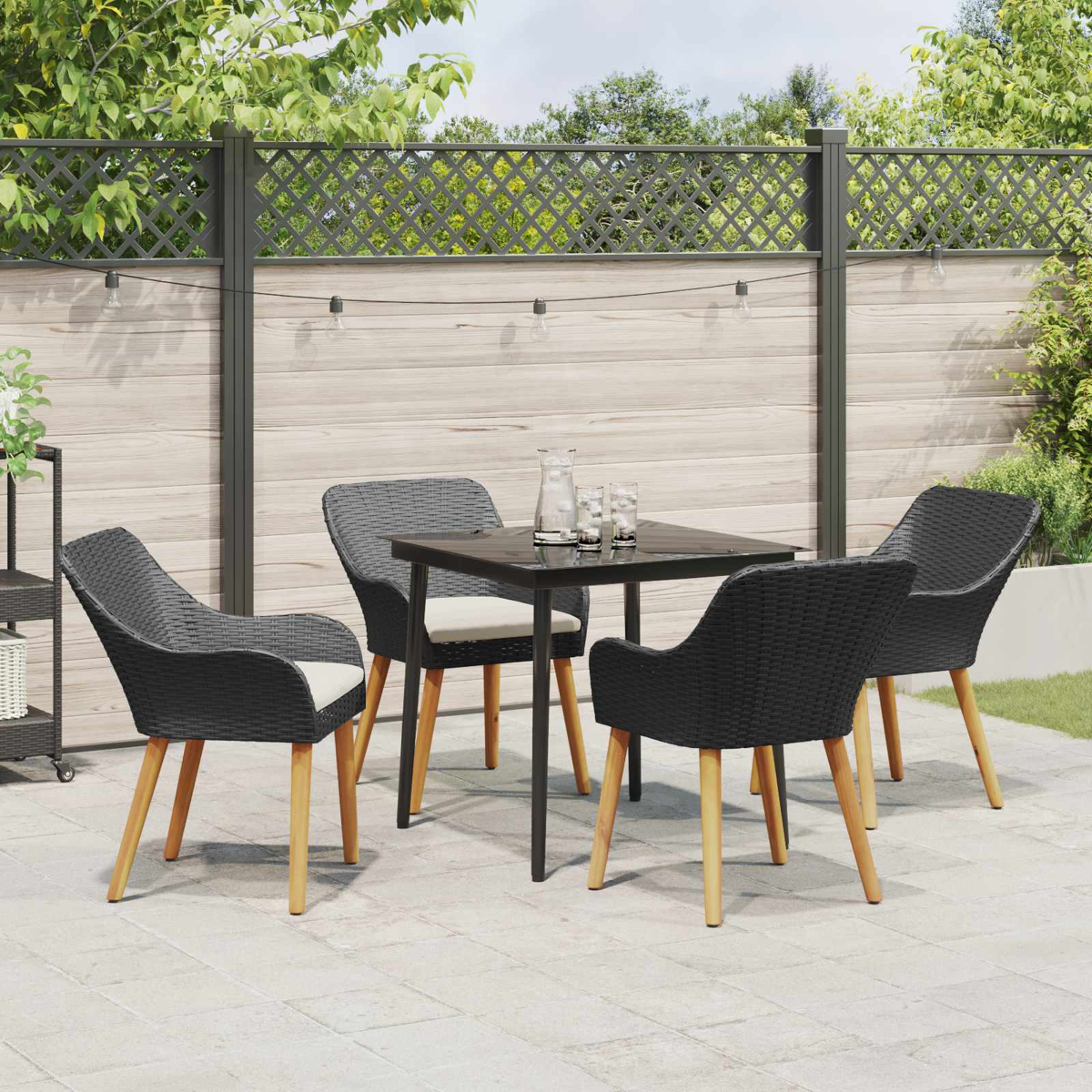 Juego de patio exterior con sillas negras, mesa y patas de madera clara. Contra una valla de madera y vegetación.