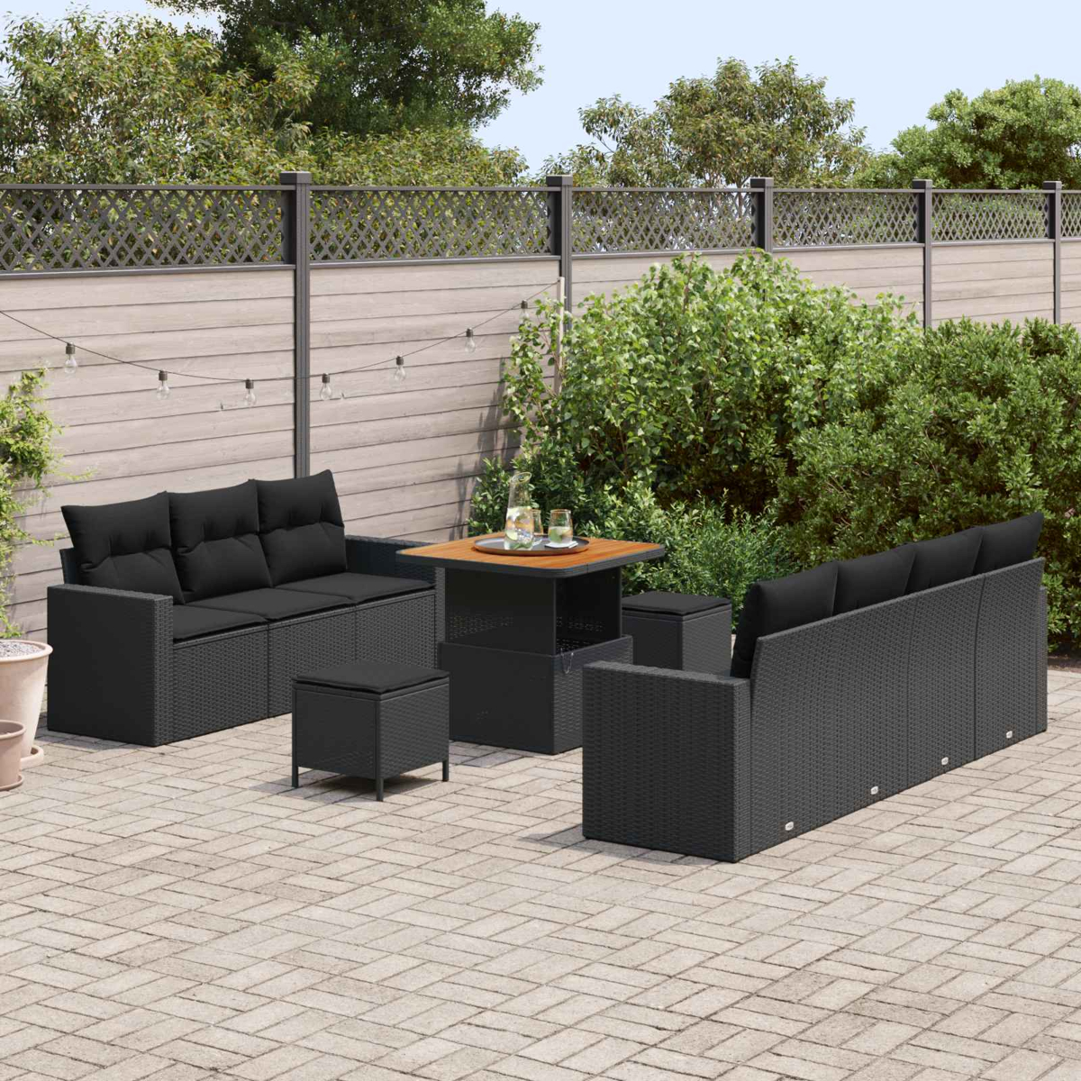 Terrassenmöbel-Set mit schwarzem Korbmöbel, Sofas, Ottomanen und Tisch auf Backsteinpflaster mit Zaun.