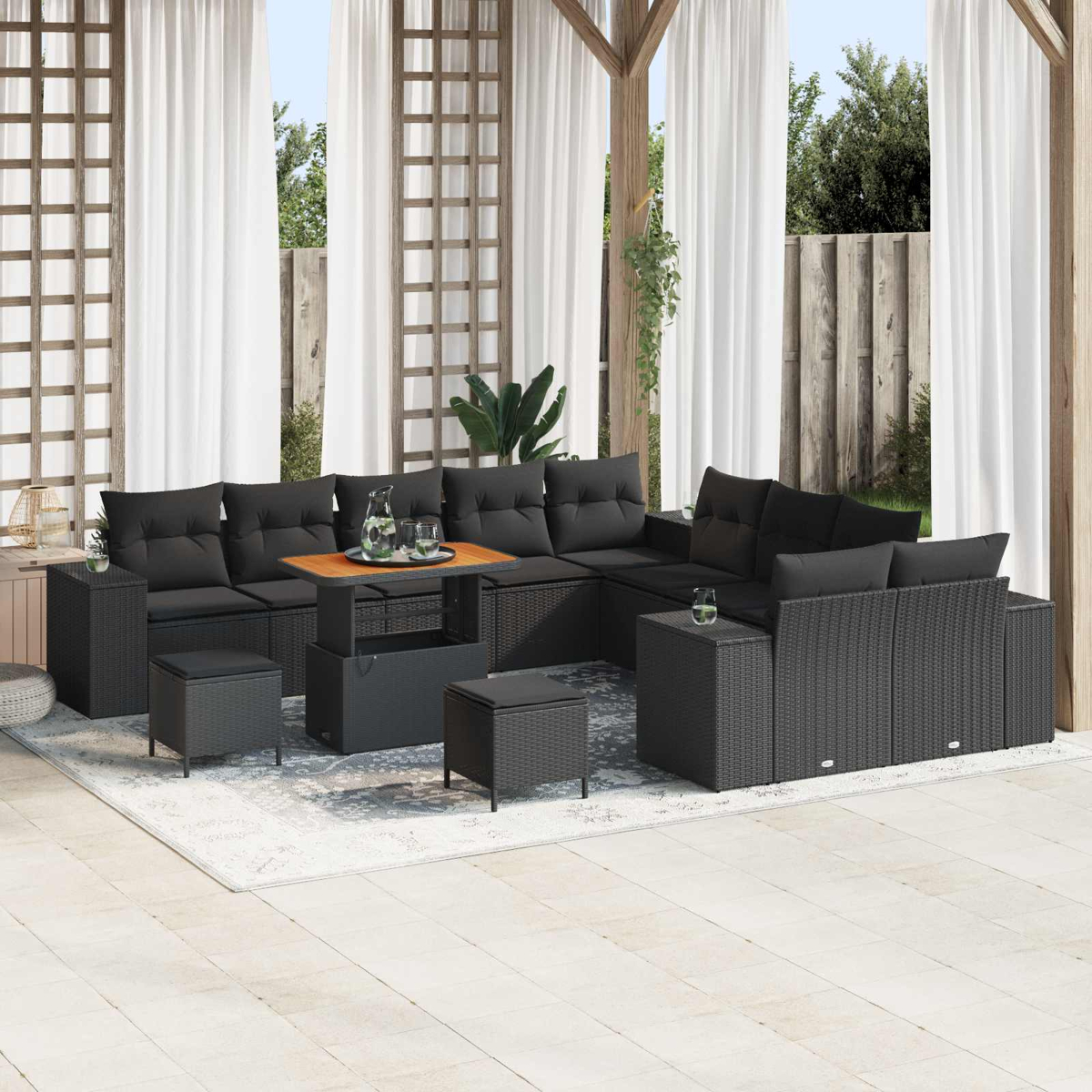 Outdoor-Ecksofa mit schwarzen Kissen, Holztisch und Hockern. Weiße Vorhänge und eine Holzkonstruktion im Hintergrund.