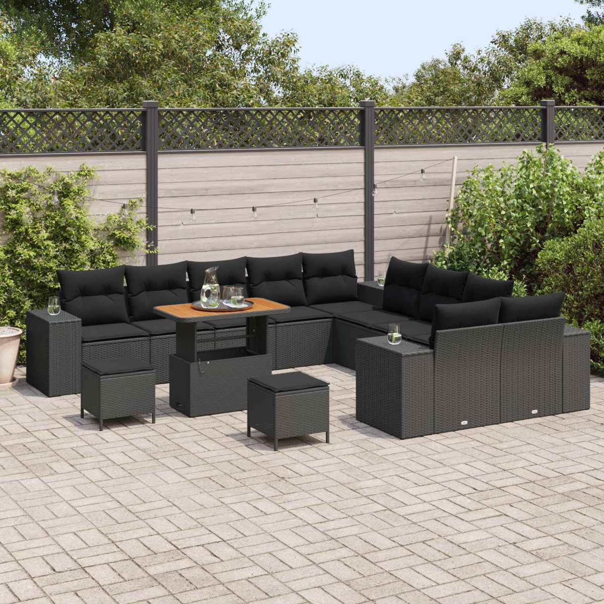 Schwarzes Outdoor-Sofa aus Korbgeflecht mit Holztisch, zwei Hockern und einem Beistelltisch. Auf einer Ziegelterrasse mit Zaun.