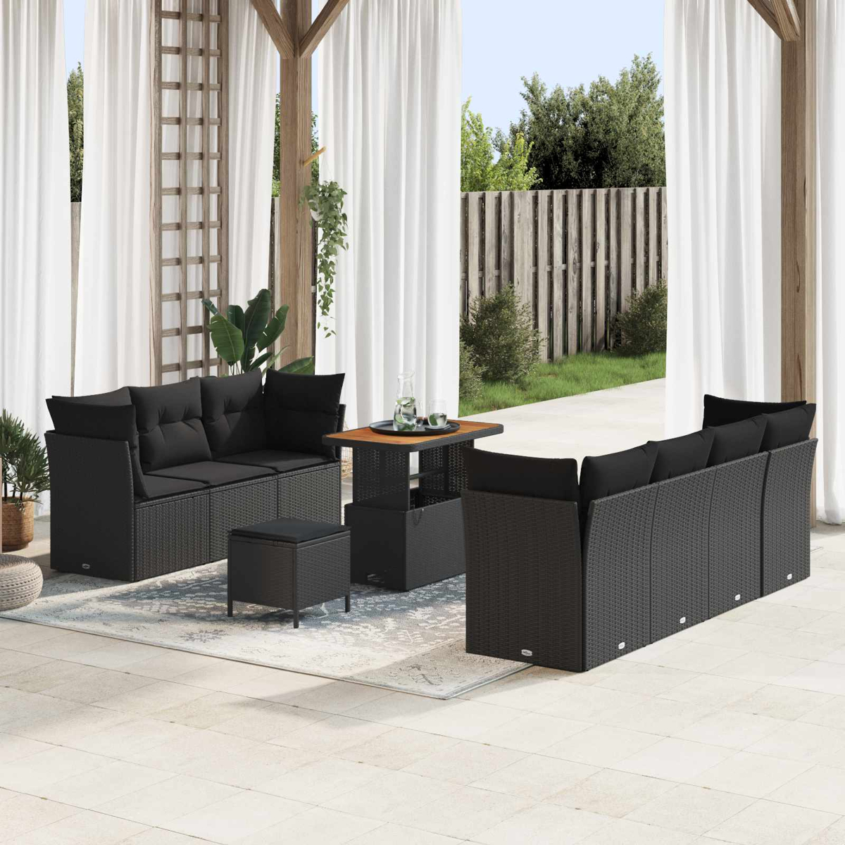 Set patio esterno con mobili in vimini neri, un tavolino e tende bianche sullo sfondo, giornata di sole.