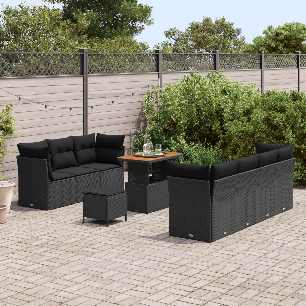 Set per patio esterno con mobili in vimini neri, tra cui un divano, un pouf e un tavolo, su un patio in pietra.