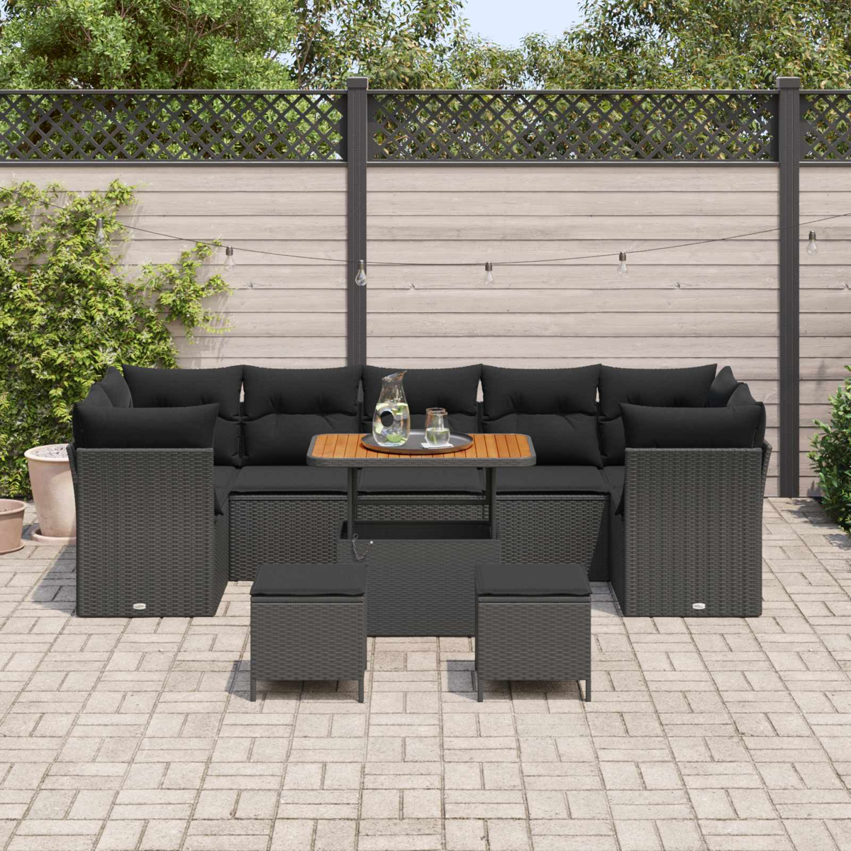 Terrassengarnitur mit schwarzen Kissen, Tisch mit Tablett und zwei Hockern. Holzzaun im Hintergrund.