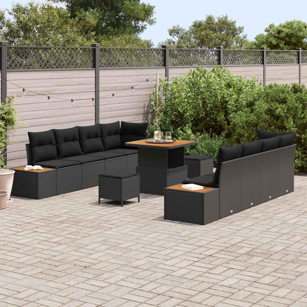 Gartenmöbel-Set mit schwarzen Kissen und einem Holztisch. Auf einer Ziegelterrasse mit Holzzaun und Grünanlage.
