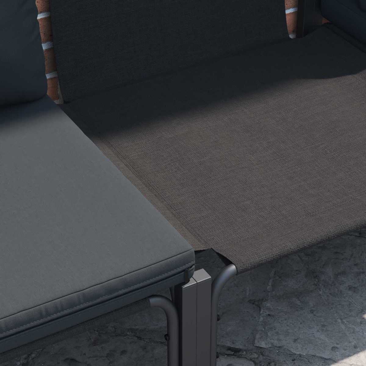 Primo piano di una sedia a sdraio da patio grigio scuro con un muro di mattoni sullo sfondo. La sedia ha un cuscino e una seduta in rete.
