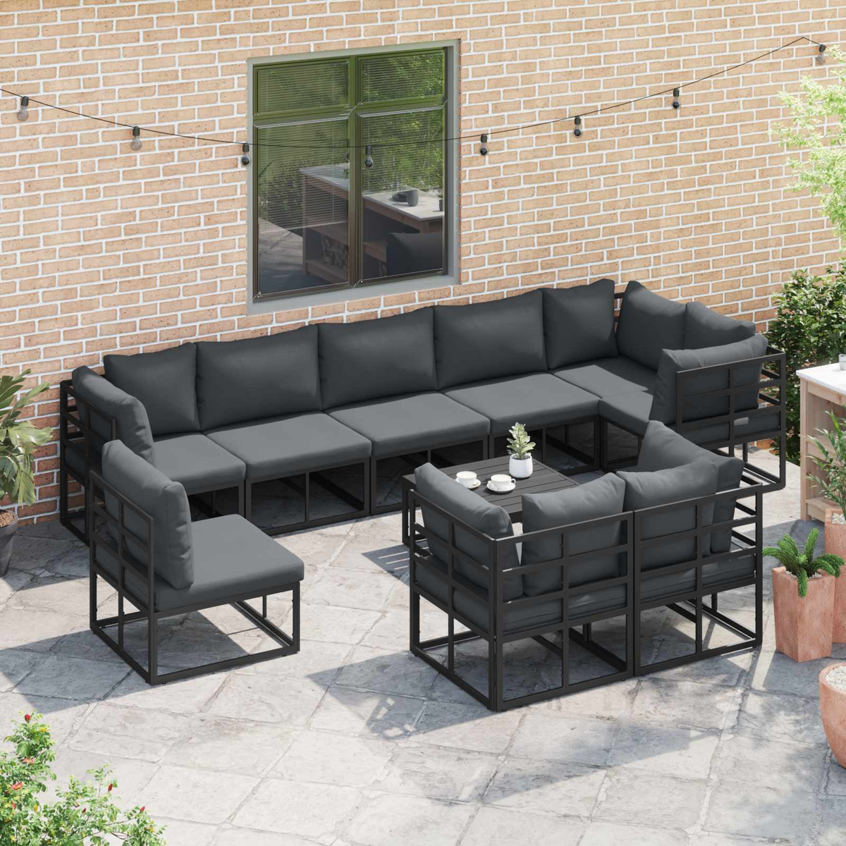 Outdoor-Ecksofa mit grauen Kissen auf einer Steinterrasse. Ziegelmauer im Hintergrund mit Fenster und Lichterketten.