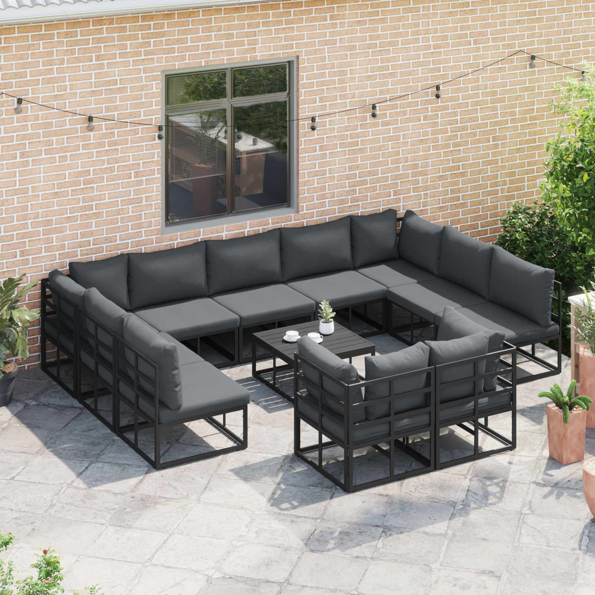 Outdoor-Ecksofa mit grauen Kissen auf einer Terrasse. Enthält einen kleinen Tisch und Pflanzen, vor einer Backsteinmauer.