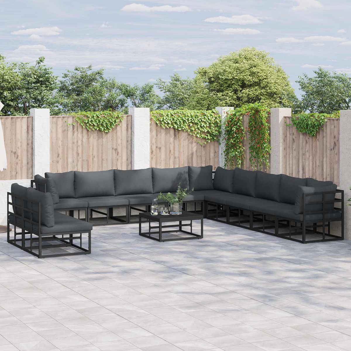 Garten-Terrassenset mit dunkelgrauen Kissen. Enthält ein Ecksofa, Sessel und einen Couchtisch auf einer gefliesten Terrasse.
