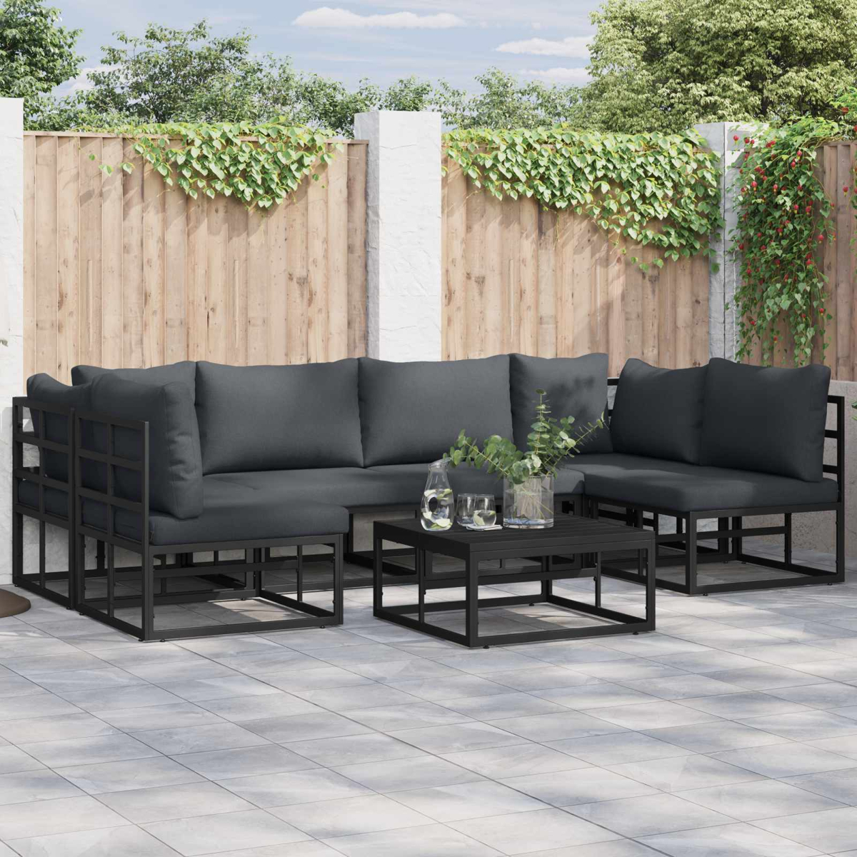 Gartenmöbel-Set auf einer Terrasse. Enthält ein Ecksofa, zwei Sessel und einen Couchtisch. Dahinter ist ein Holzzaun.