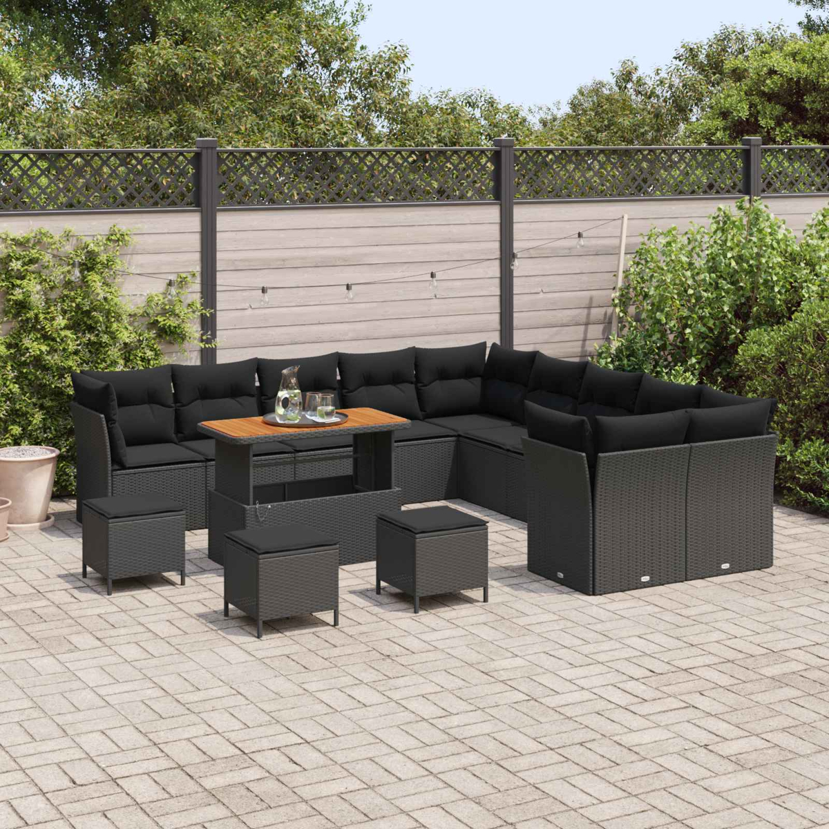 Garten-Terrassenset mit schwarzen Kissen, einem Holztisch und Hockern. Auf einer Ziegelterrasse mit Zaun und Grün.