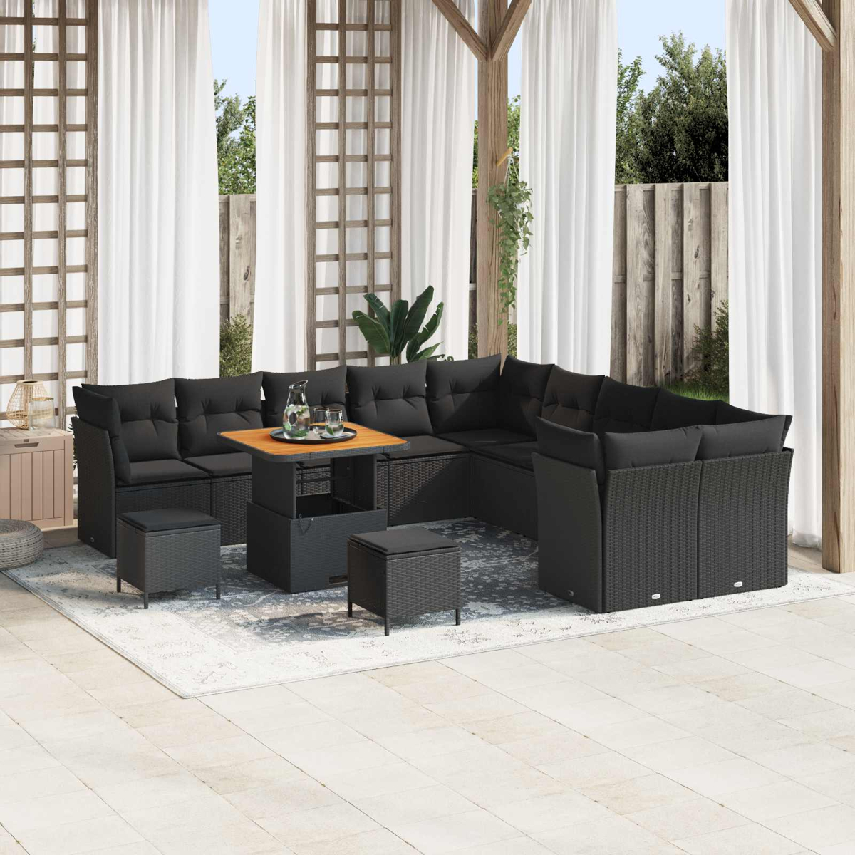 Garten-Sitzgruppe mit schwarzen Kissen, Holztisch und Hockern auf einem Teppich. Weiße Vorhänge und Holzstruktur im Hintergrund.