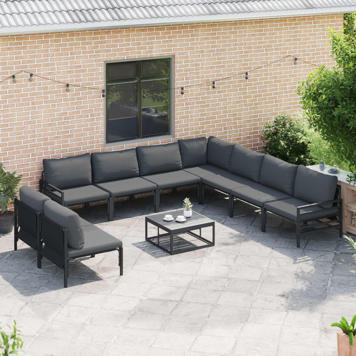 Terrassenset mit dunkelgrauen Kissen. Enthält ein Ecksofa, zwei Sessel und einen Couchtisch vor einer Backsteinmauer.