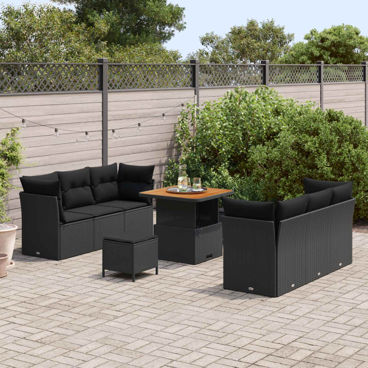 Terrassenmöbel-Set mit schwarzem Korbmöbel, schwarzen Kissen, einem quadratischen Tisch und einer gepflasterten Terrasse.