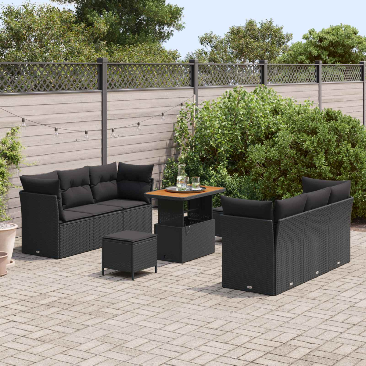 Garten-Terrassenset mit schwarzem Korbmöbeln, Sofas, Tisch mit Getränken und Hocker auf einer Steinterrasse.