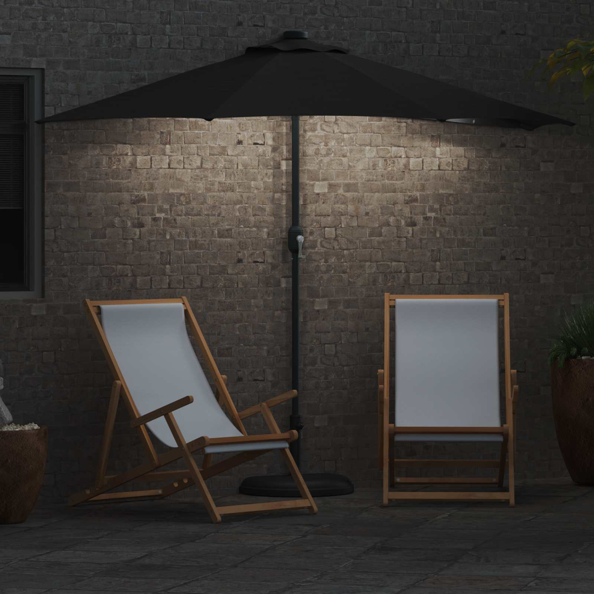 Due sedie di legno con tessuto bianco sono sotto un ombrello nero. Un muro di mattoni fa da sfondo. La scena è illuminata di notte.