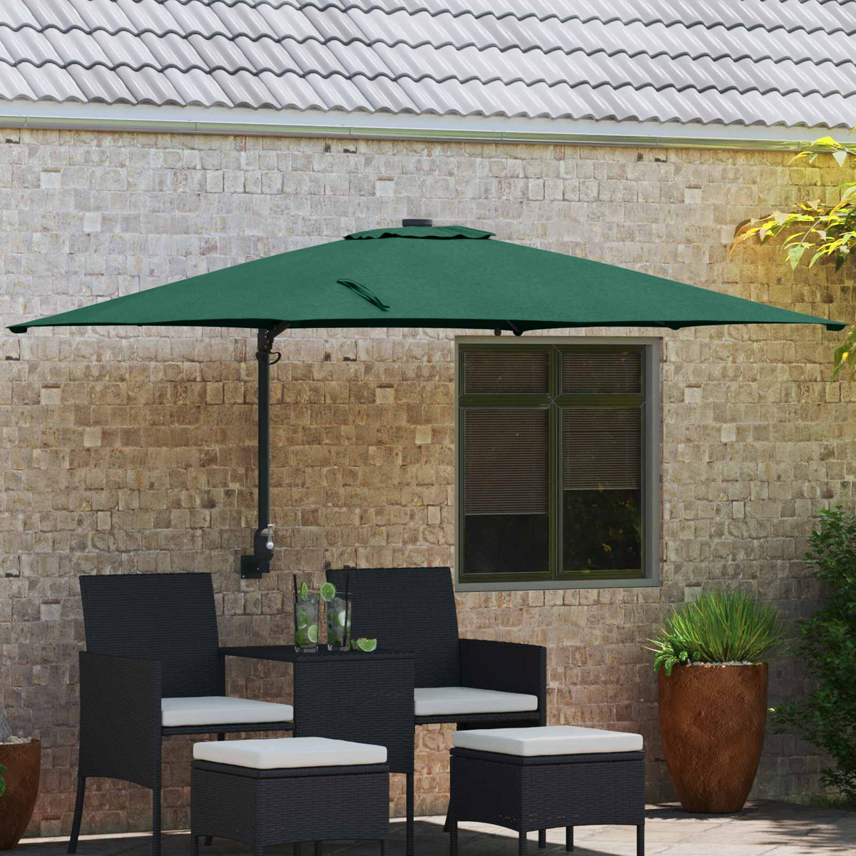 Un ombrello verde ombreggia un set da patio con due sedie, due pouf e un tavolino. Sullo sfondo una finestra e un muro di mattoni.