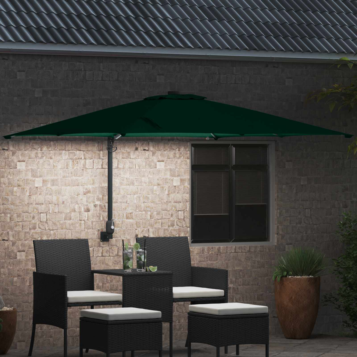 Un ombrellone da giardino verde scuro sopra un tavolo e sedie neri. I cocktail sono sul tavolo. Un muro di mattoni fa da sfondo.