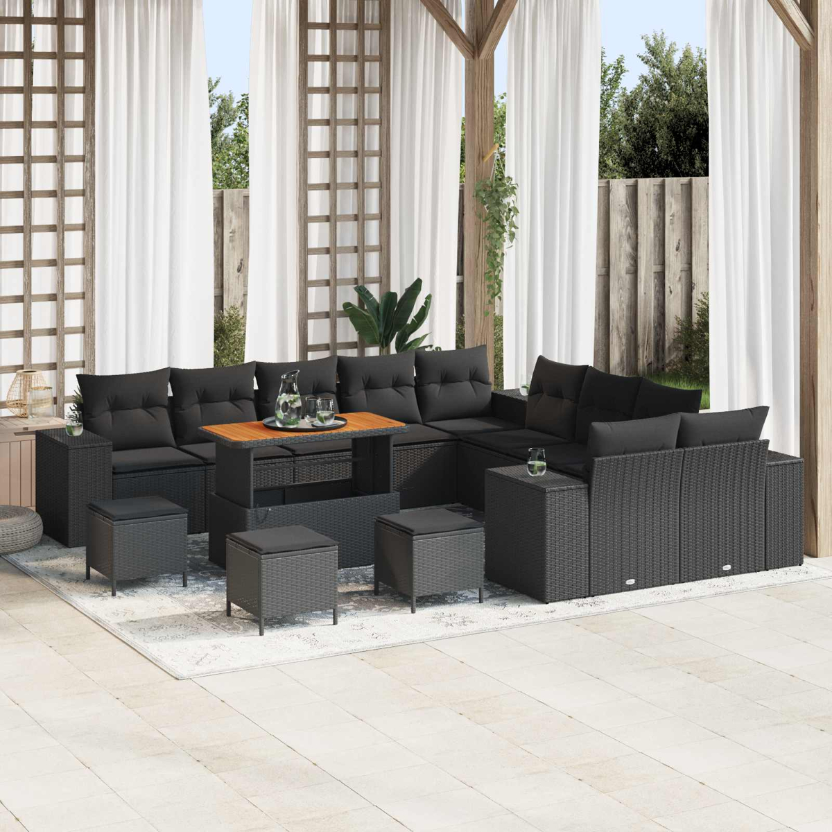 Outdoor-Terrassenset mit schwarzen Korbmöbeln, Kissen und einem Holztisch. Weiße Vorhänge und eine Gartenkulisse.