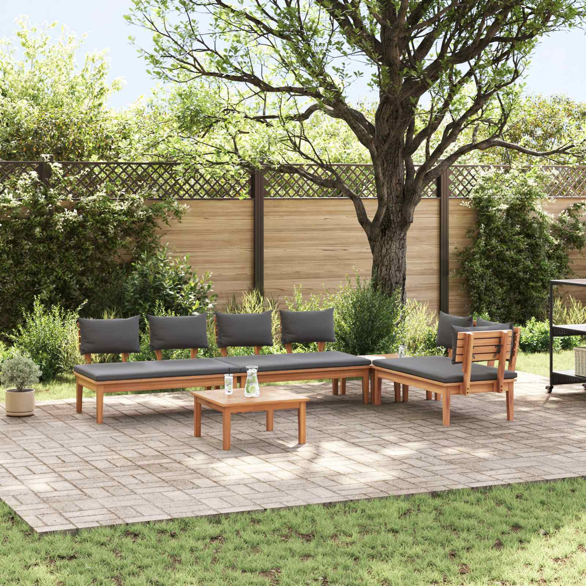 Outdoor-Sitzarrangement mit Holzmöbeln und grauen Kissen. Ein kleiner Tisch mit Getränken steht davor, umgeben von Grün.