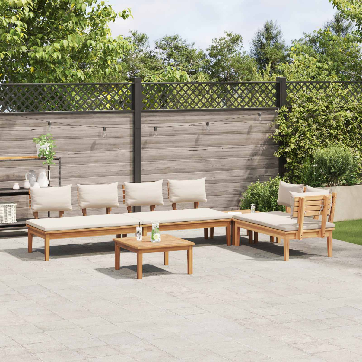 Garten-Sitzgruppe mit hellen Kissen auf einer Terrasse. Holzmöbel umfassen ein Sofa, Stühle und einen kleinen Tisch. Grün im Hintergrund.