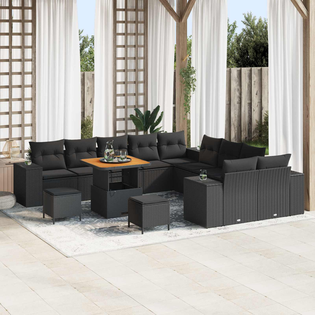 Garten-Sitzgruppe mit schwarzen Kissen, Holztisch und Hockern. Weiße Vorhänge und Holzstruktur im Hintergrund.