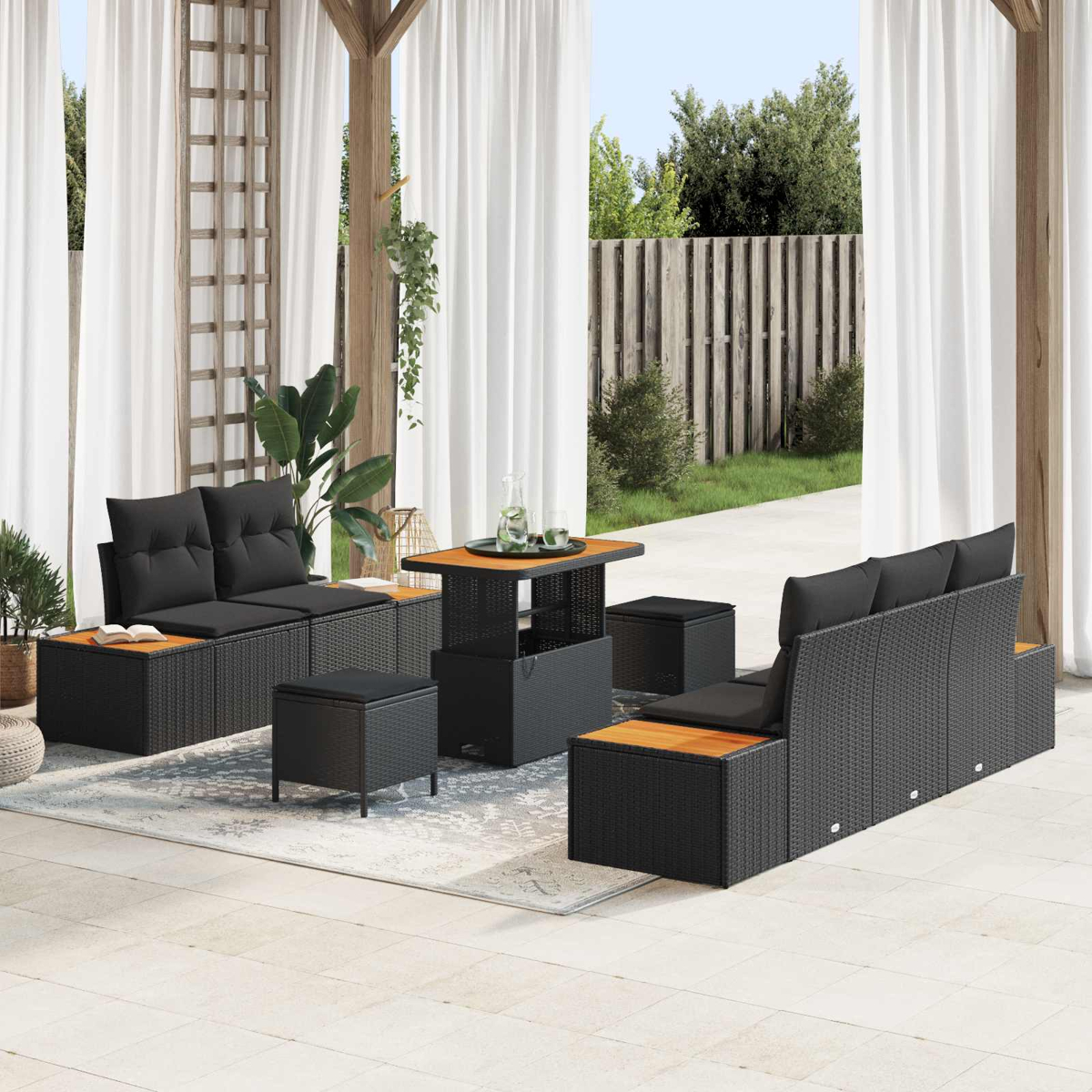 Gartenmöbel-Set mit schwarzen Sofas, Holztischen und Kissen. Weiße Vorhänge und Holzzaun im Hintergrund.