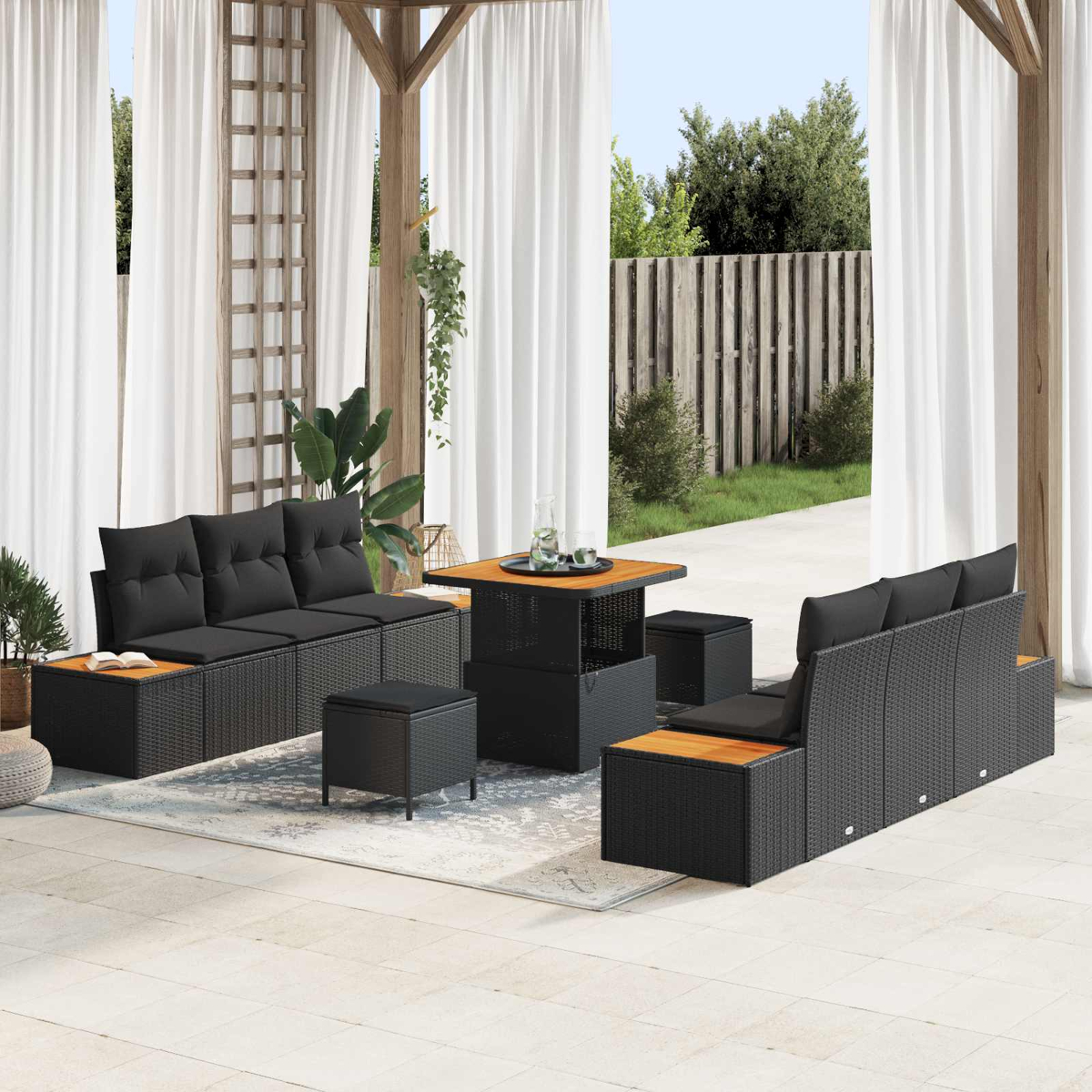 Gartenmöbel-Set. Schwarze Sofas, Ottomanen und ein Tisch mit Holzplatte. Weiße Vorhänge und grüne Blätter sind sichtbar.
