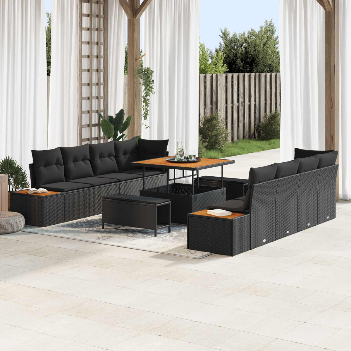Terrassenmöbel-Set mit schwarzem Korbmöbeln, Kissen und einem Holztisch. Weiße Vorhänge und Garten im Hintergrund.