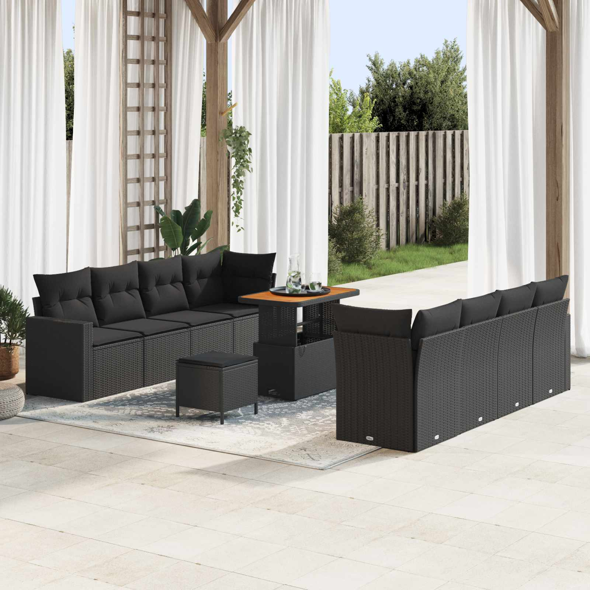 Garten-Terrassenset mit schwarzem Korbmöbel, Tisch und Hocker. Weiße Vorhänge und eine Holzstruktur im Hintergrund.
