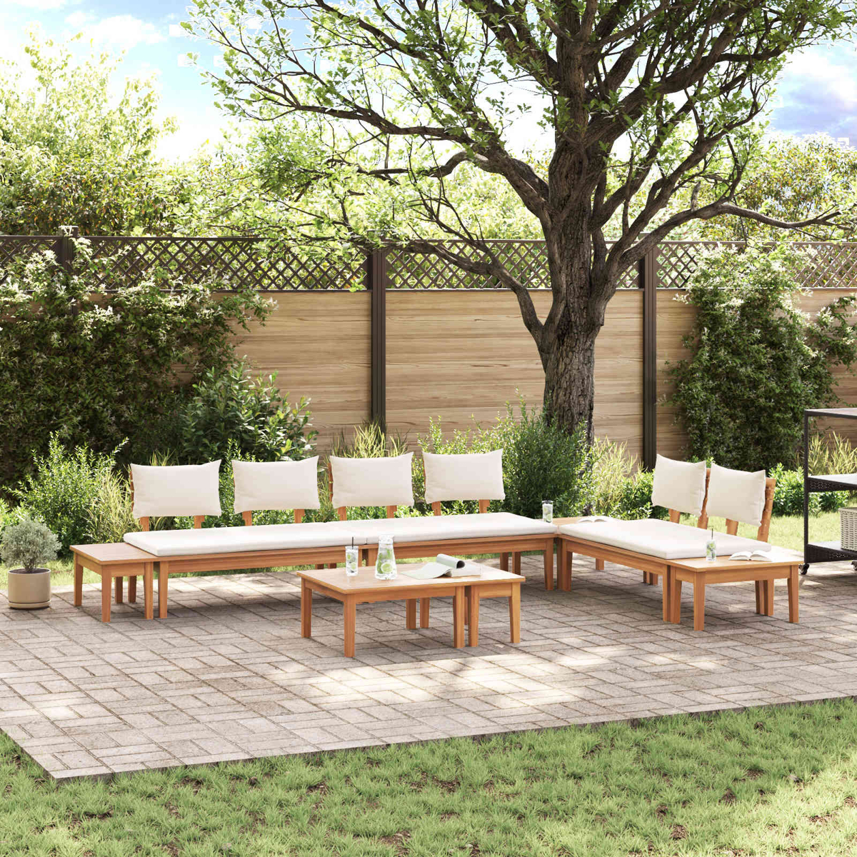 Gartenbestuhlung mit Holzbänken und Tischen auf einer Terrasse. Großer Baum im Hintergrund, blauer Himmel.