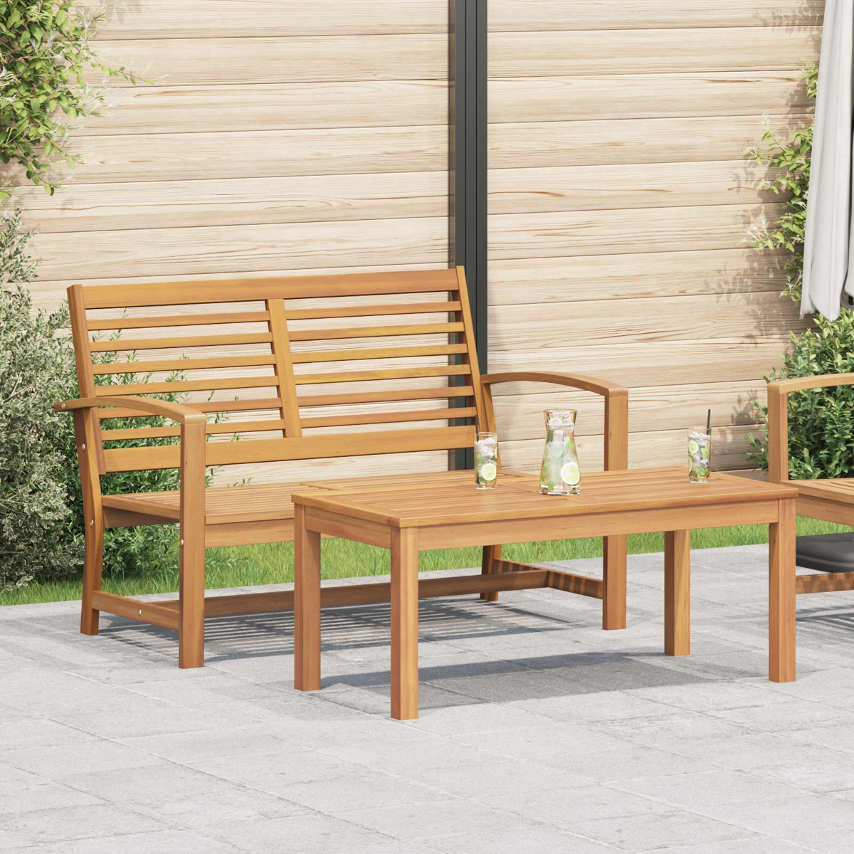 Holz-Gartensitzgruppe. Eine Bank, ein Tisch und ein Stuhl stehen auf einer Terrasse, Getränke auf dem Tisch. Dahinter ein Holzzaun.