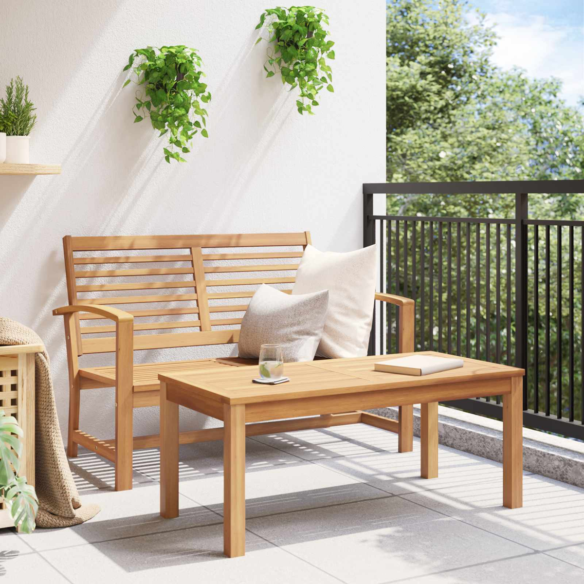 Holzbank und Tisch auf einem Balkon. Kissen, Pflanzen und ein Glas Wasser sind sichtbar. Grüne Bäume sind im Hintergrund.