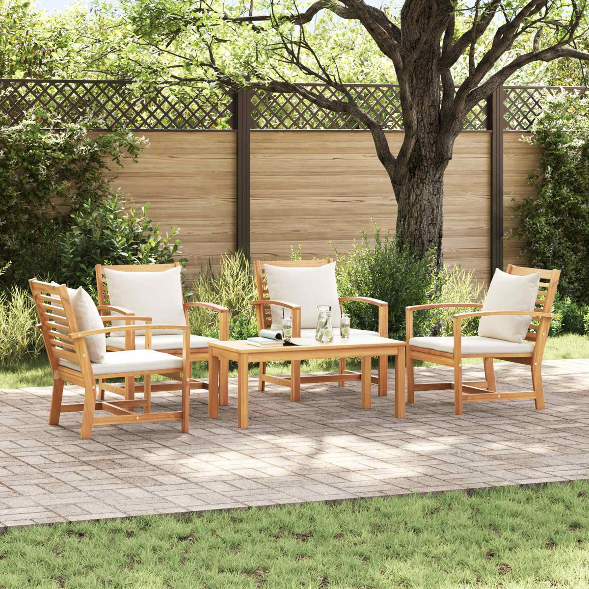 Garten-Sitzgruppe mit Holzstühlen und weißen Kissen, die um einen Tisch auf einer Ziegelstein-Terrasse angeordnet sind. Im Hintergrund ist ein Holzzaun zu sehen.