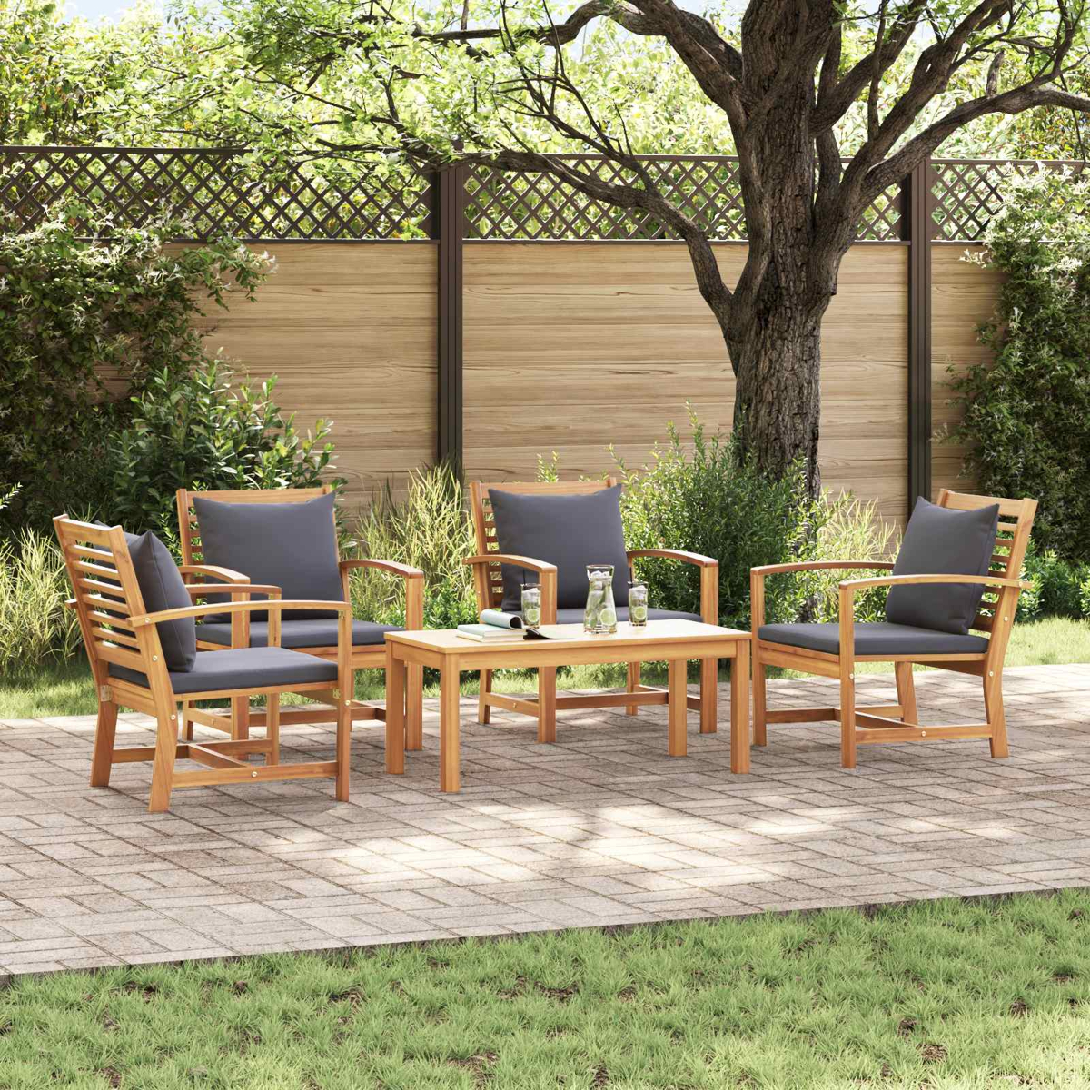 Gartenmöbel-Set mit Holzstühlen, grauen Kissen und kleinem Tisch. Auf einer Backsteinterrasse mit Holzzaun und Baum im Hintergrund.