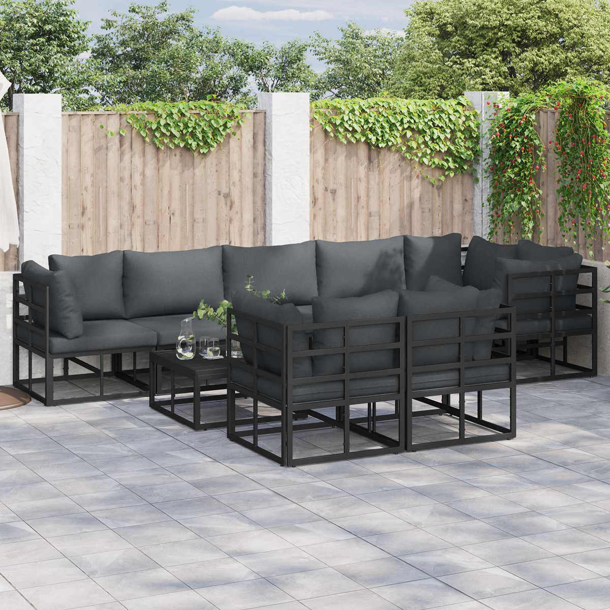 Terrassenmöbel-Set mit dunkelgrauen Kissen. Enthält ein Ecksofa, Stühle und einen kleinen Tisch auf einer gefliesten Terrasse.