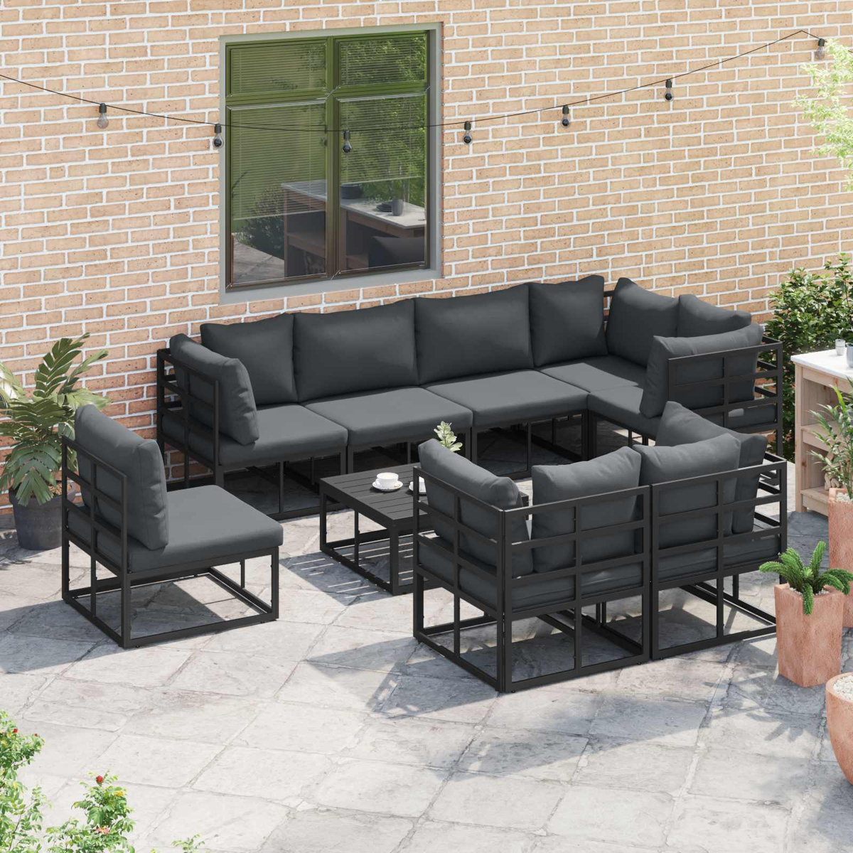 Terrassenset mit dunkelgrauen Kissen. Enthält ein Ecksofa, Stühle und einen Couchtisch vor einer Backsteinmauer.